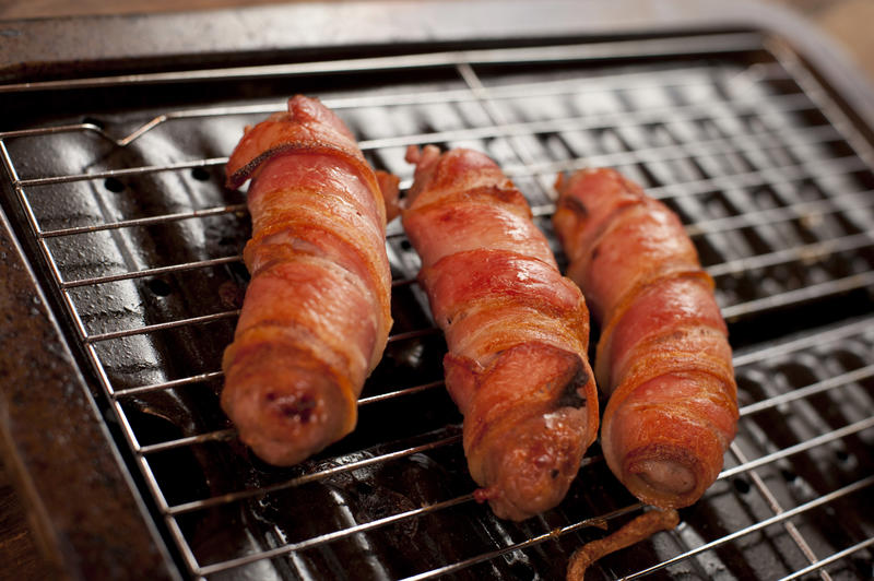 A close up of cooked, crispy pigs in blankets on an oven tray.