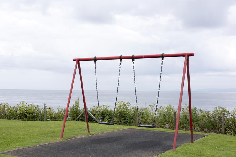 Coastal empty A-frame swings on a kids playground overlooking the ocean on a cloudy cold day