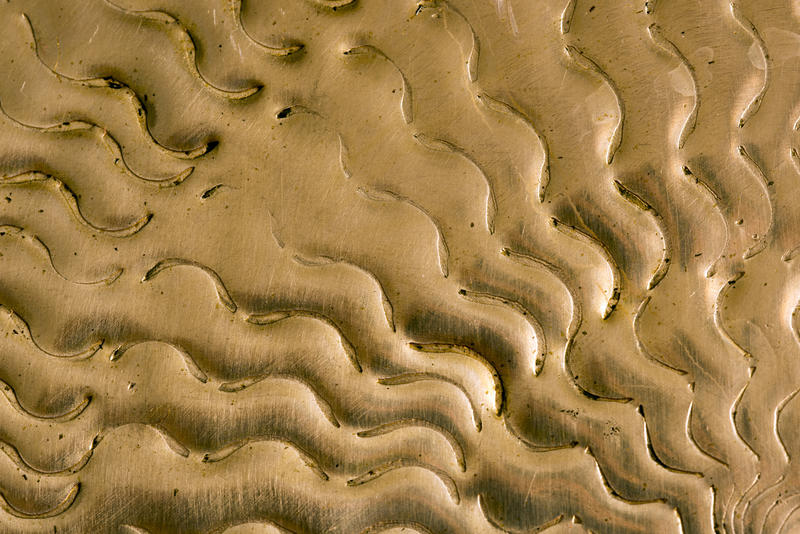 Wavy undulating pattern pressed into brass emanating from the right bottom corner in a full frame background texture