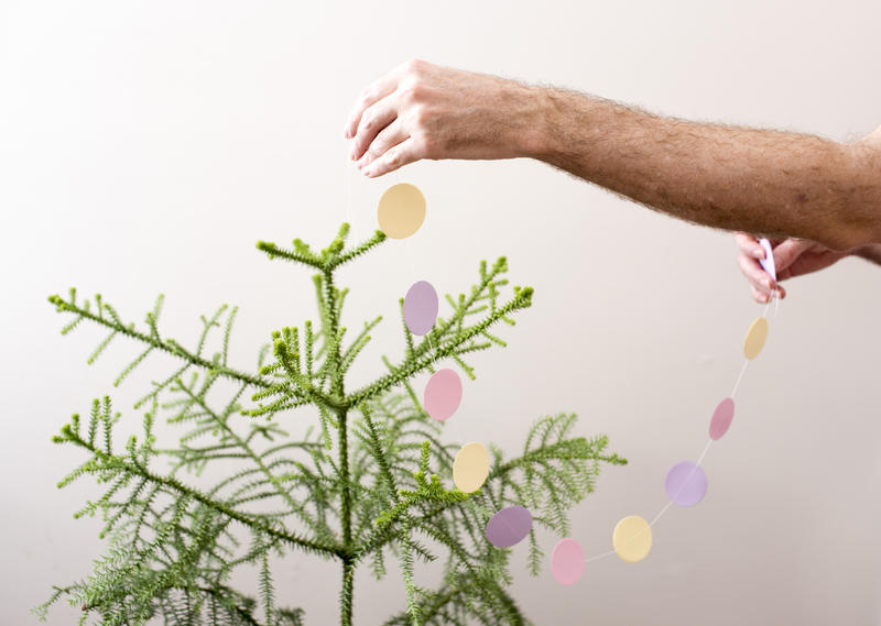 hands reaching out an putting a pretty pastel coloured paper garland onto a christmas tree