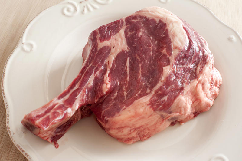 A close up of a raw rib eye steak on a white, porcelain plate.