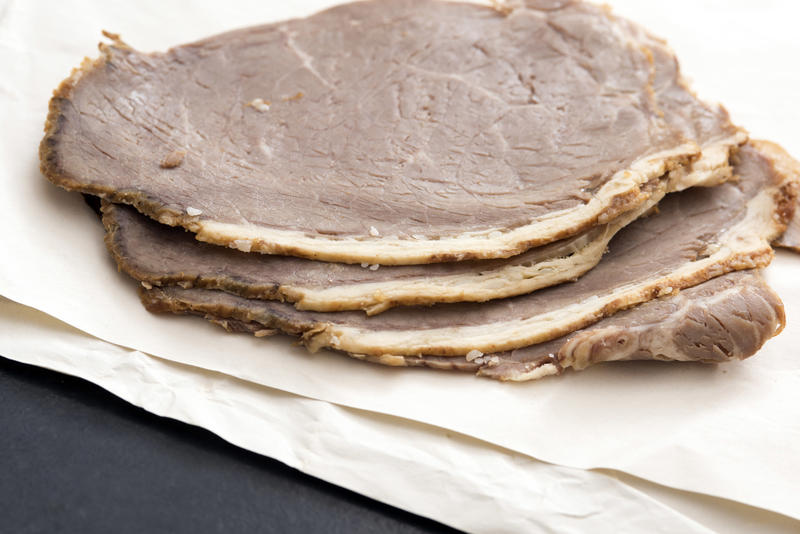 Sliced roast beef in close-up on white paper on kitchen table