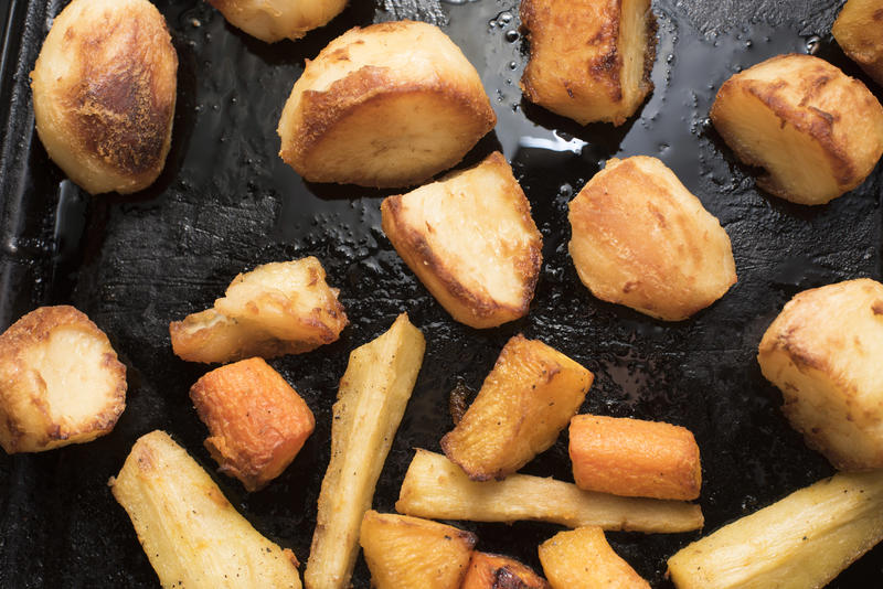 Roasting potatoes and vegetables with oil on black pan, viewed in close-up from above