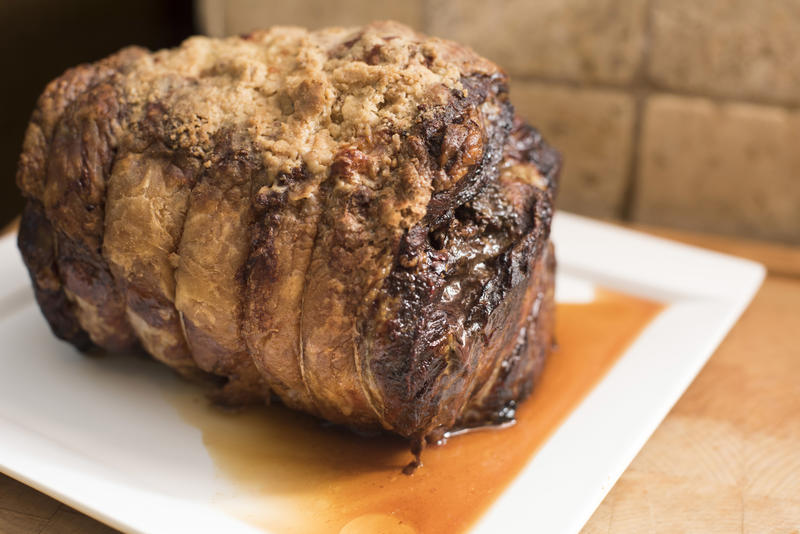 Whole trussed seasoned roasted beef joint served on a plate with meat juice in a close up side view