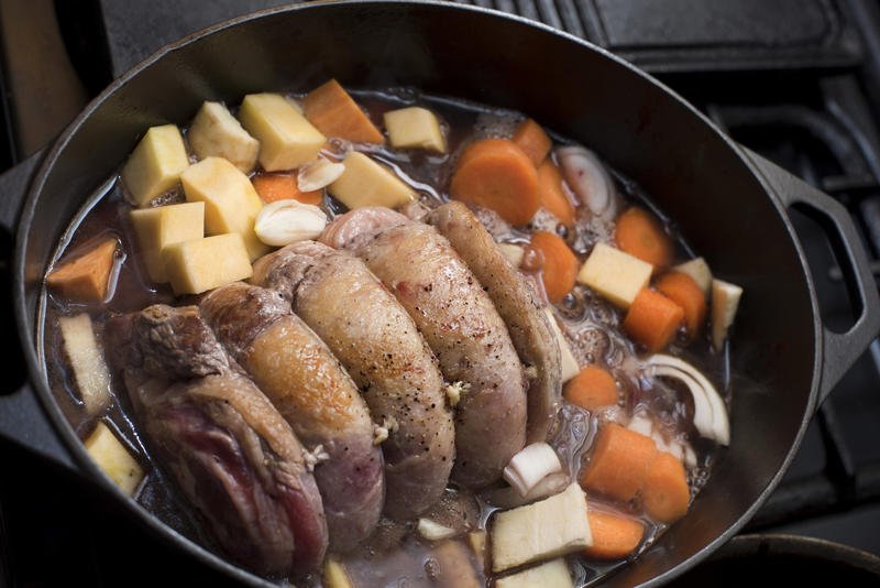 A close up of a trussed, beef shoulder simmering in a pot with assorted vegetables.