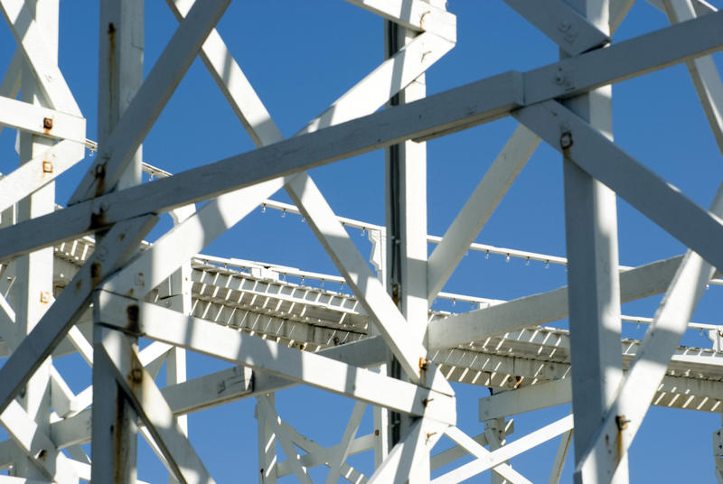 Close up detail of the metal support frame of a rollercoaster track against a sunny blue sky at an amusement park