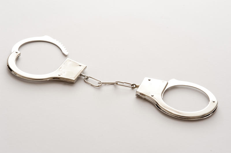 Silver half-open handcuffs on white table surface viewed in close-up. Security or release concept