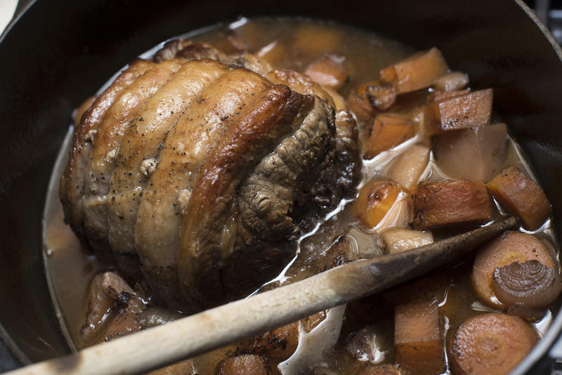 Cooking a shoulder of beef in a casserole simmering it with assorted fresh vegetables in a pot in a close up high angle view