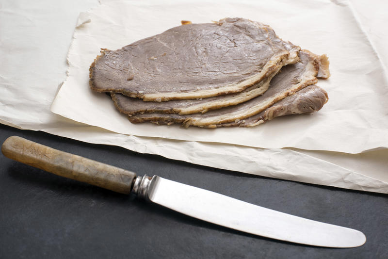 Sliced roast beef on a paper and kitchen knife, viewed in close-up