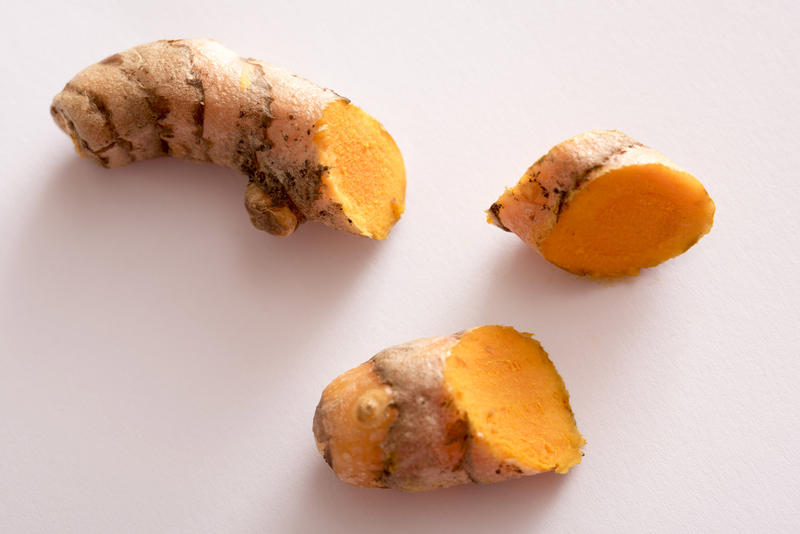 Pieces of sliced turmeric in close-up on white surface, viewed from above