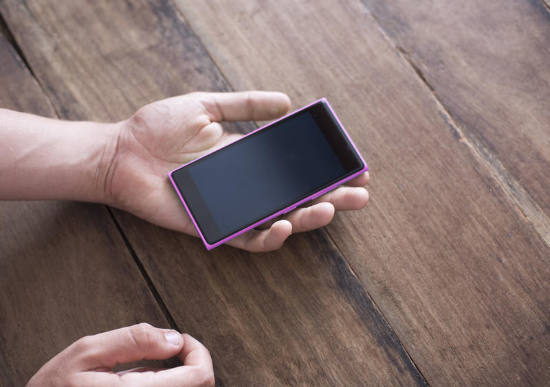 Man holding a blank black smartphone in his hand as he sits at a wooden table waiting for an incoming text message in a close up view