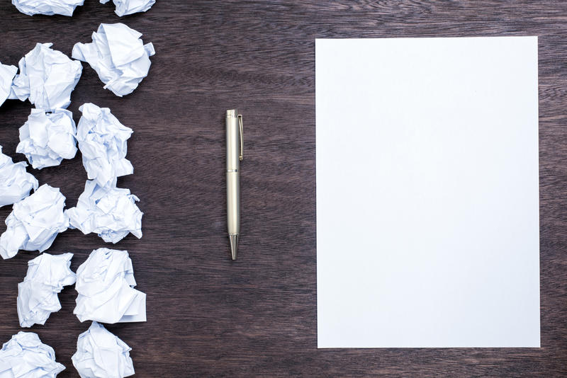 Starting Afresh concept with a sheet of clean white paper and pen alongside rows of crumpled discarded pages on a wooden desk