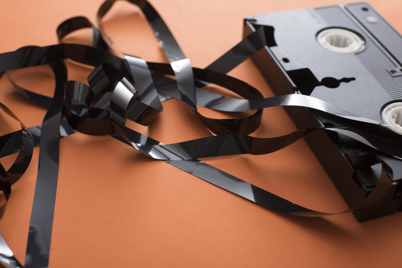VHS cassette with tangled tape in close-up on orange table surface