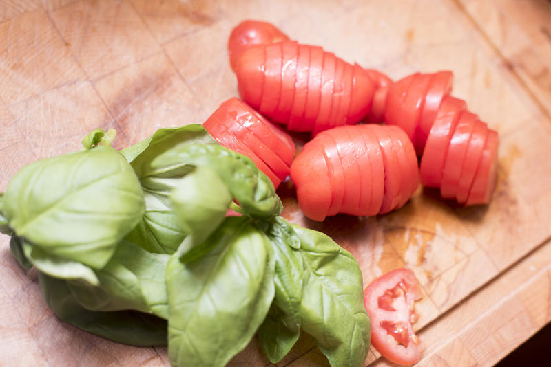 Sliced tomato and fresh basil on a chopping board ready for use in a salad, Mediterranean or Italian cooking