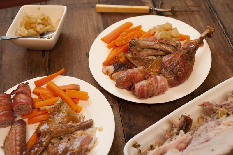 Two servings of Turkey roast dinner with vegetables and bacon rolls for Thanksgiving on a wooden table with side dishes