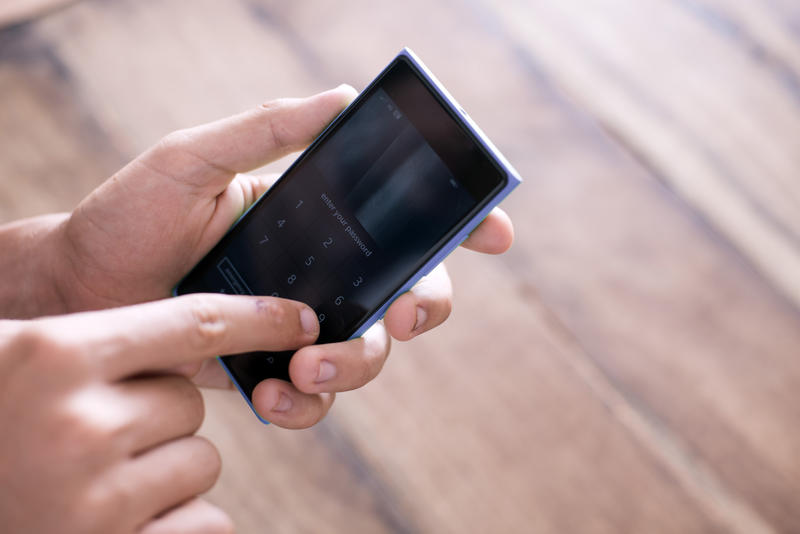 Man using the touch screen on his smartphone typing in information with his finger in a close up view of his hands over a wood background with copy space