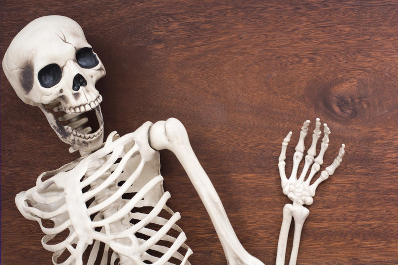a happy looking skeleton on a wooden surface, waving a boney hand