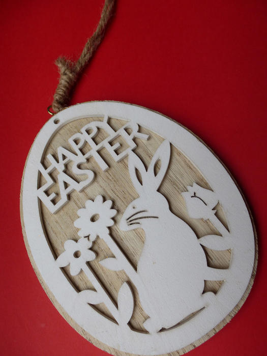 Happy Easter carved wooden pendant with a rabbit among flowers, viewed in close-up on red background