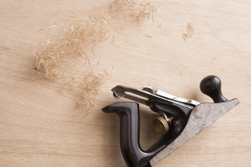 Woodworking plane on a planed wood panel surrounded by loose sawdust with copy space