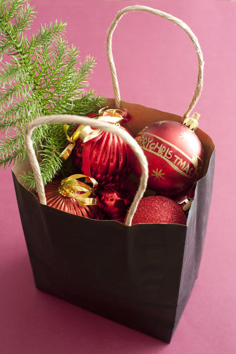 Paper store carrier bag full of Christmas decorations with assorted red balls and a green pine tree over a festive red background viewed high angle