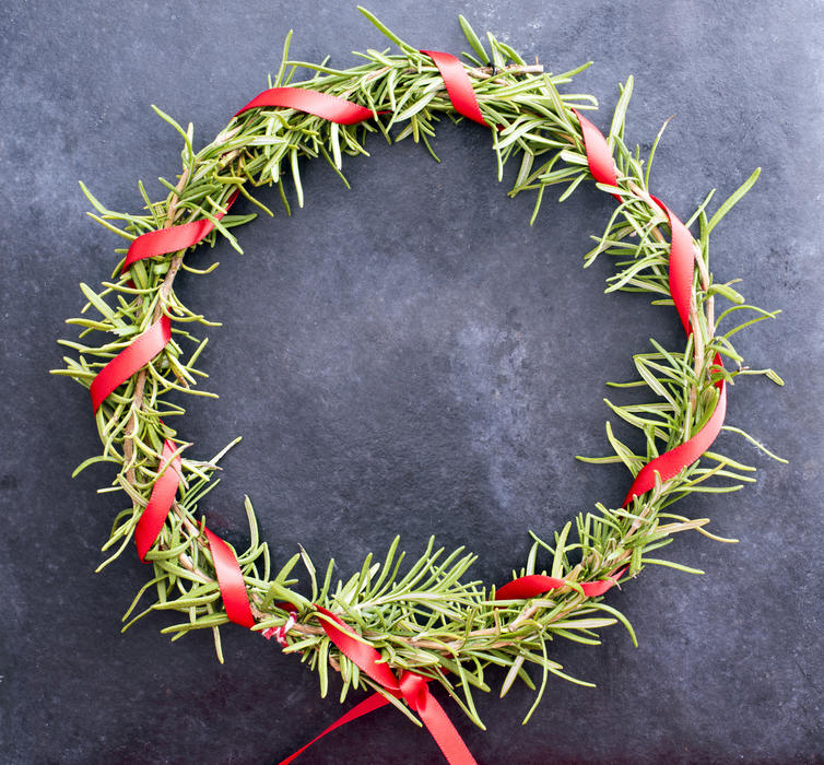 Colourful homemade pine Christmas wreath with a twisted red ribbon around the foliage over a dark background with copy space for a card