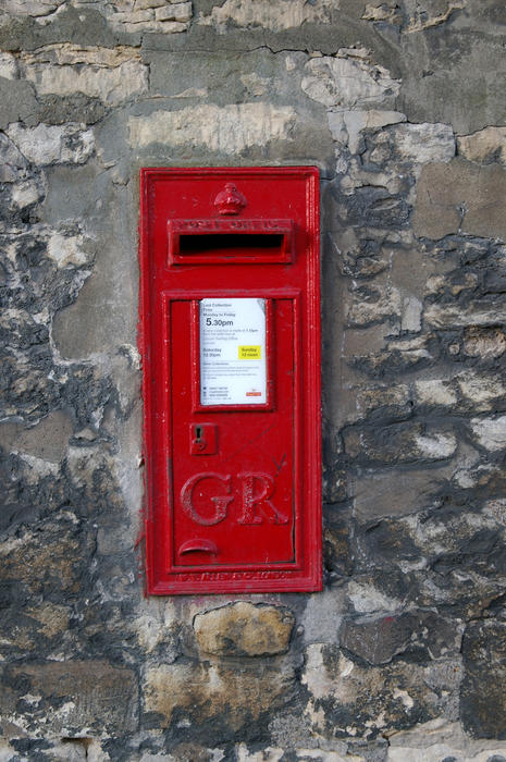 a red uk posting box mounted in a stone wall