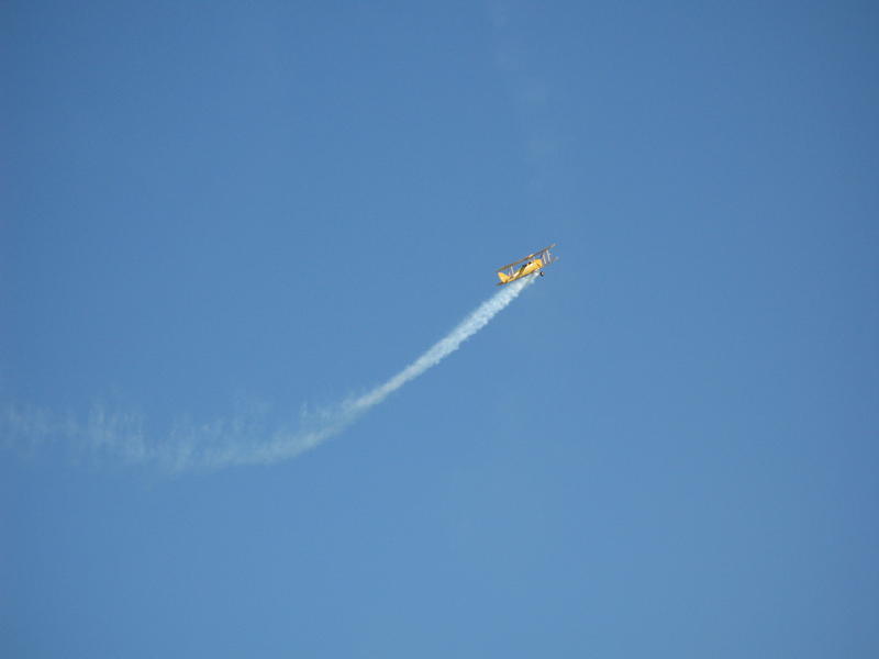 a yellow stunt plane with a trail of smoke