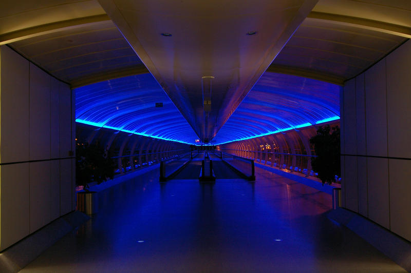 a blue lit walkway between terminals at manchester airport, uk