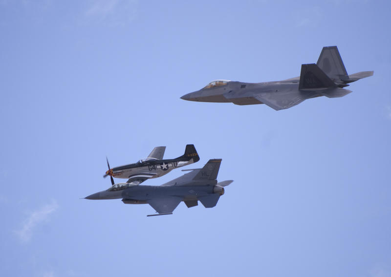 three planes in flight, an on P-51 mustang with propeller, and modern FA18 hornet and F22 raptor jet aircraft