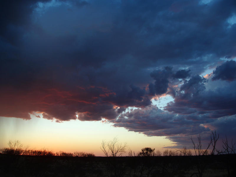 a storm cloud bearing rain over a flat desert landscape after sunset