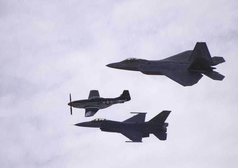 an airshow formation of three different aircraft, a P-51 mustang propeller plane, and modern FA18 and F22 jet aircraft