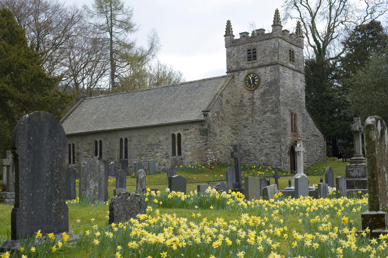 the outside of a small village church with springtime daffodils in the churchyard