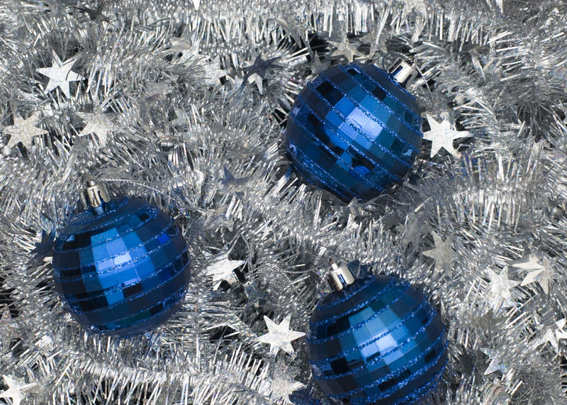 three metallic blue christmas baubles on a silver tinsel backdrop