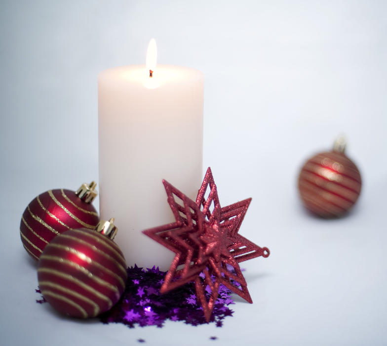 a still life of a lit christmas candle and decorations on a bright light background