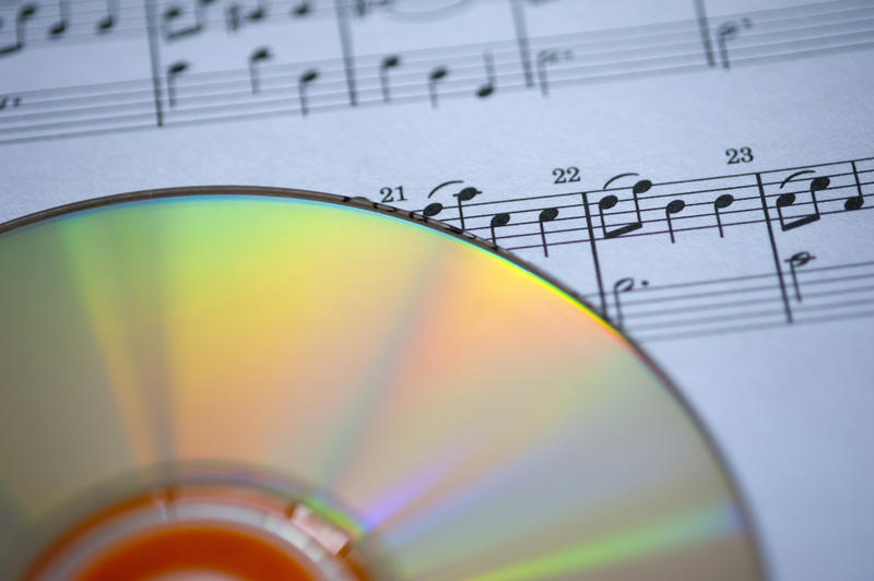 multicoloured reflectings from the surface of a CD, pictured with a narrow depth of field against a background of sheet music
