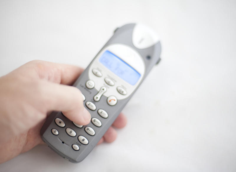 a hand dialing a number of a cordless telephone