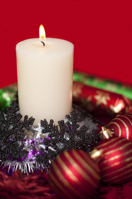 a still life of a lit christmas candle and decorations on a bright red backdrop
