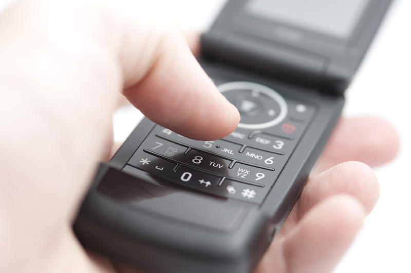holding a black coloured flip phone with thumb about to press a button on the keypad