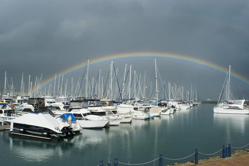 a rainbow and dark storm clouds over yachts in a marina