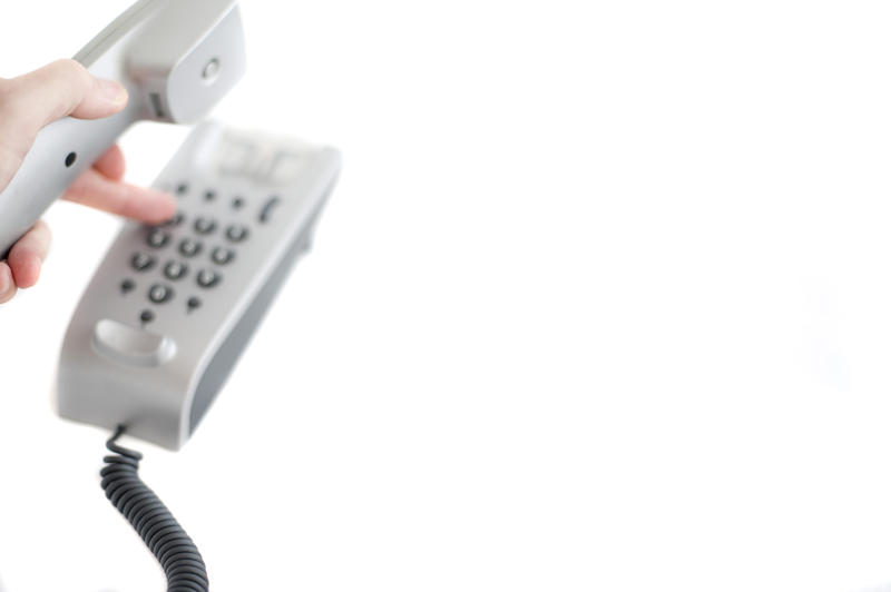 a hand dialing a number of a push button phone pictured in a high key style with a narrow depth of field