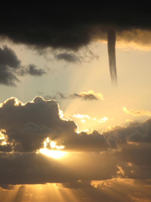 A cold air funnel dropping from the base of a dark storm cloud