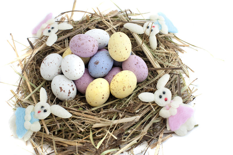 Straw nest filled with colourful sugar candy Easter Eggs and decorated with four Easter bunnies