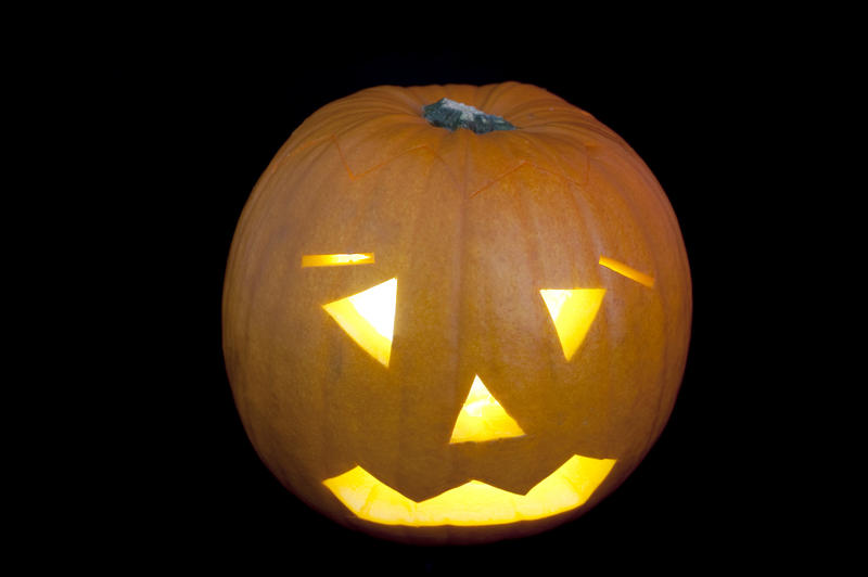 a halloween pumpkin lantern with a glowing light inside on a back backdrop