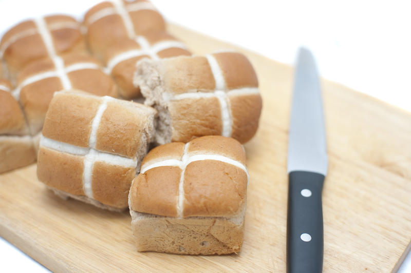 Fresh batch of Easter Hot Cross Buns on a wooden board with a knife