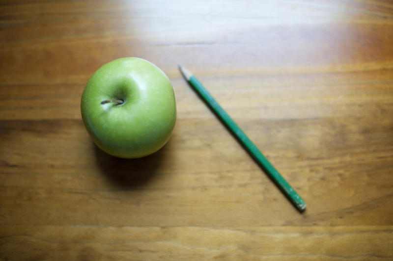 Fresh green apple and a pencil lying together on a wooden tabletop with copyspace for a learning or business background