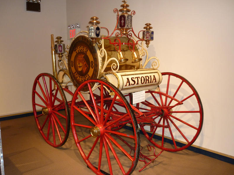 Old antique Astoria fire cart with metal spoked wheels, brass coachwork and an ornate drum and wheel enclosing the fire hose