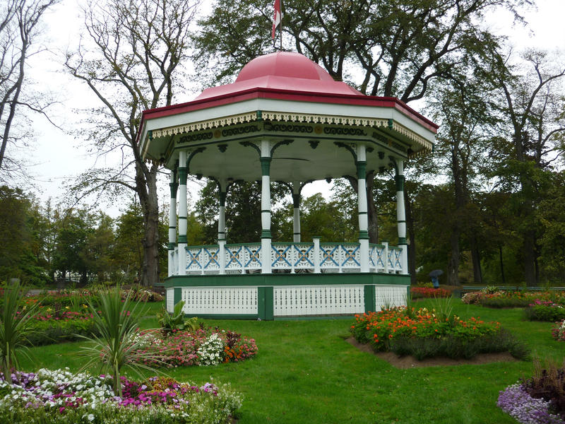 Pretty white painted bandstand or garden gazebo with a domed roof on a green lawn amongst pretty flowerbeds in a formal garden