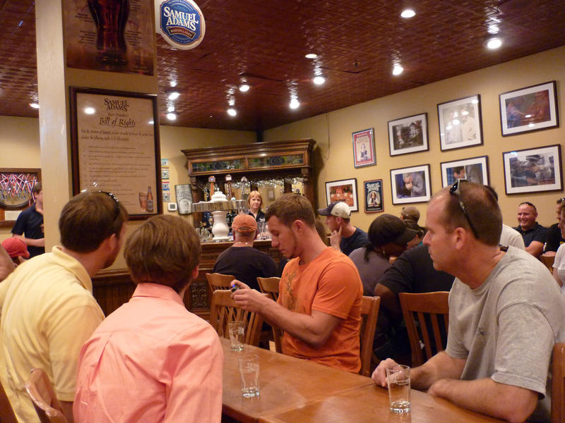 Interior of a pub or bar with young men sitting at a counter relaxing drinking their alcoholic beverages and seating tables in the background
