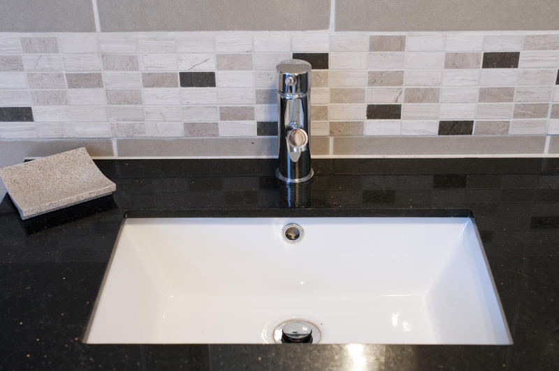 Square bathroom sink surrounded by black marble and small wall tiles