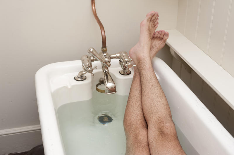 Cropped view of a man relaxing having a bath with his feet resting up on the rim of the bathtub
